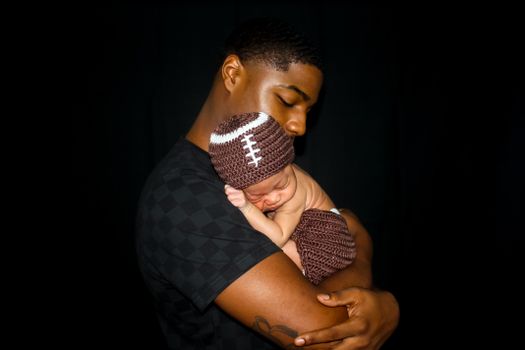 Intimate portrait of a father lovingly holding his sleeping baby against a black background.
