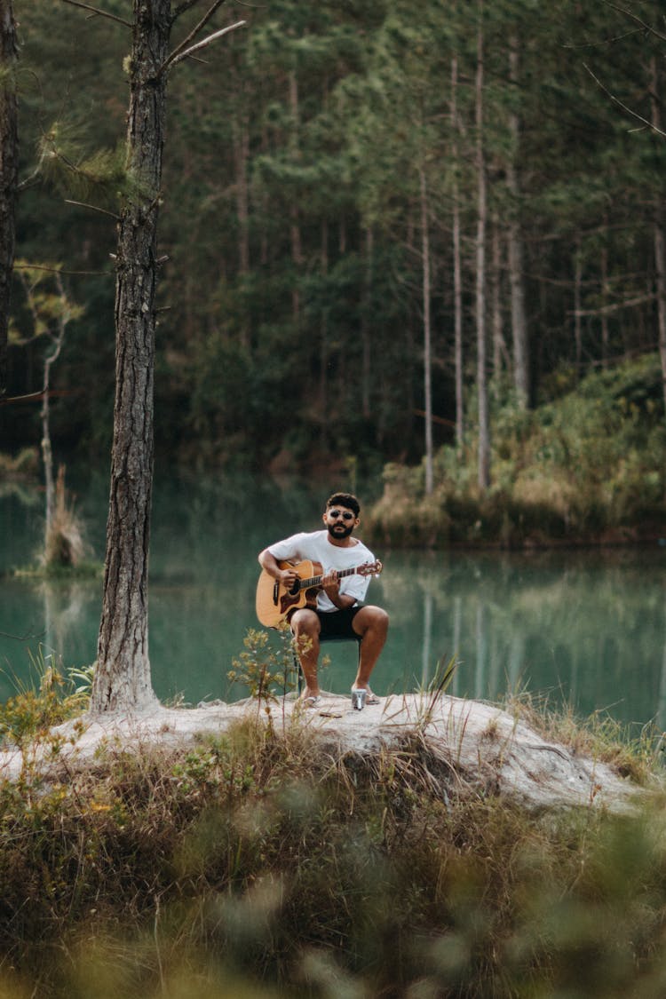 Brunette Man Playing Acoustic Guitar By Lake In A Forest