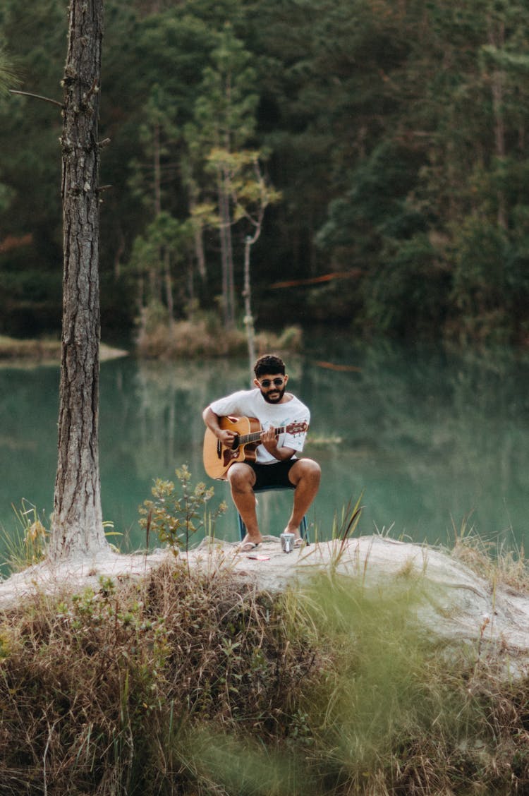 Brunette Man Playing Acoustic Guitar By Lake In A Forest