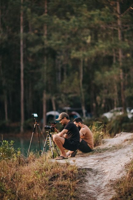 Two men sitting lakeside with cameras capturing a scenic view, surrounded by nature and tranquility.