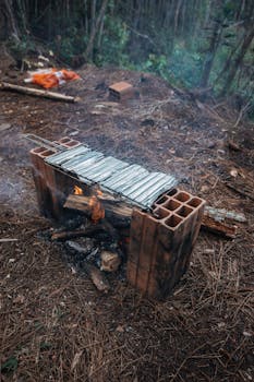 Rustic campfire grill arrangement using cinder blocks in a forest setting with pine needles.