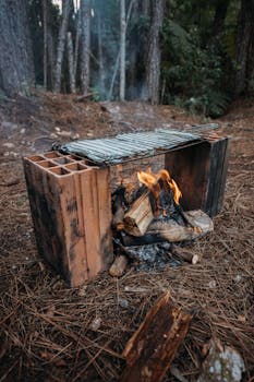 A cozy campfire setup in a forest with firewood and grill for outdoor cooking.