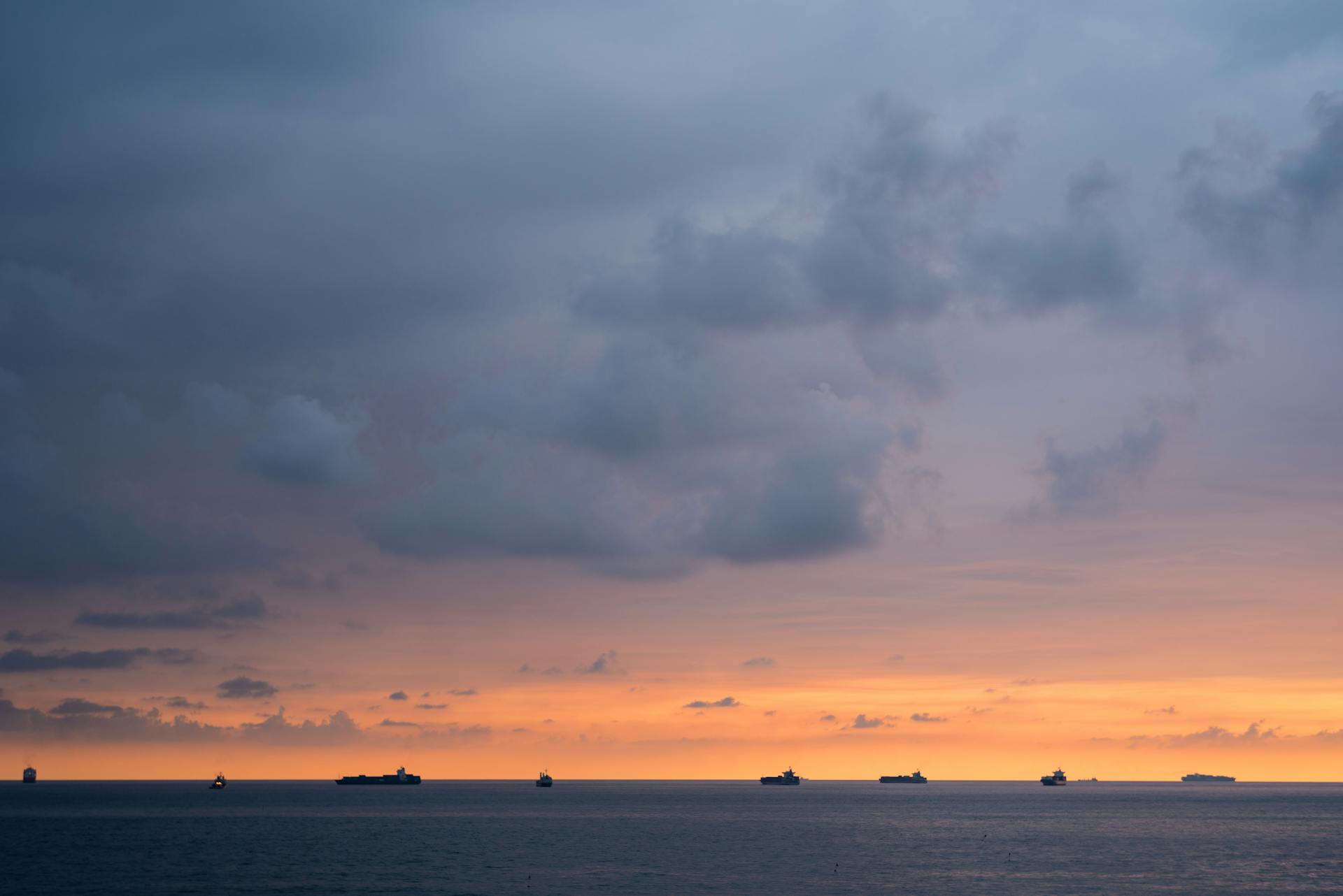 Serene ocean view at sunset with ships silhouetted against a dramatic sky.