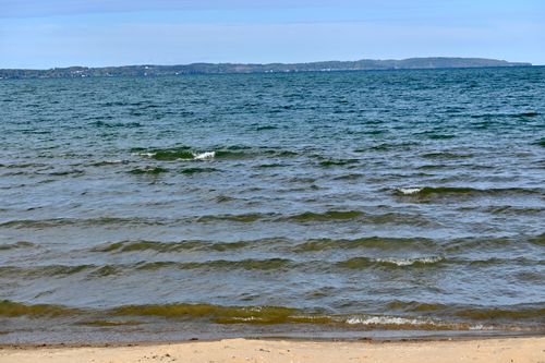 Free Experience the tranquility of a serene shoreline with gentle waves lapping at the sandy beach under a clear blue sky. Stock Photo