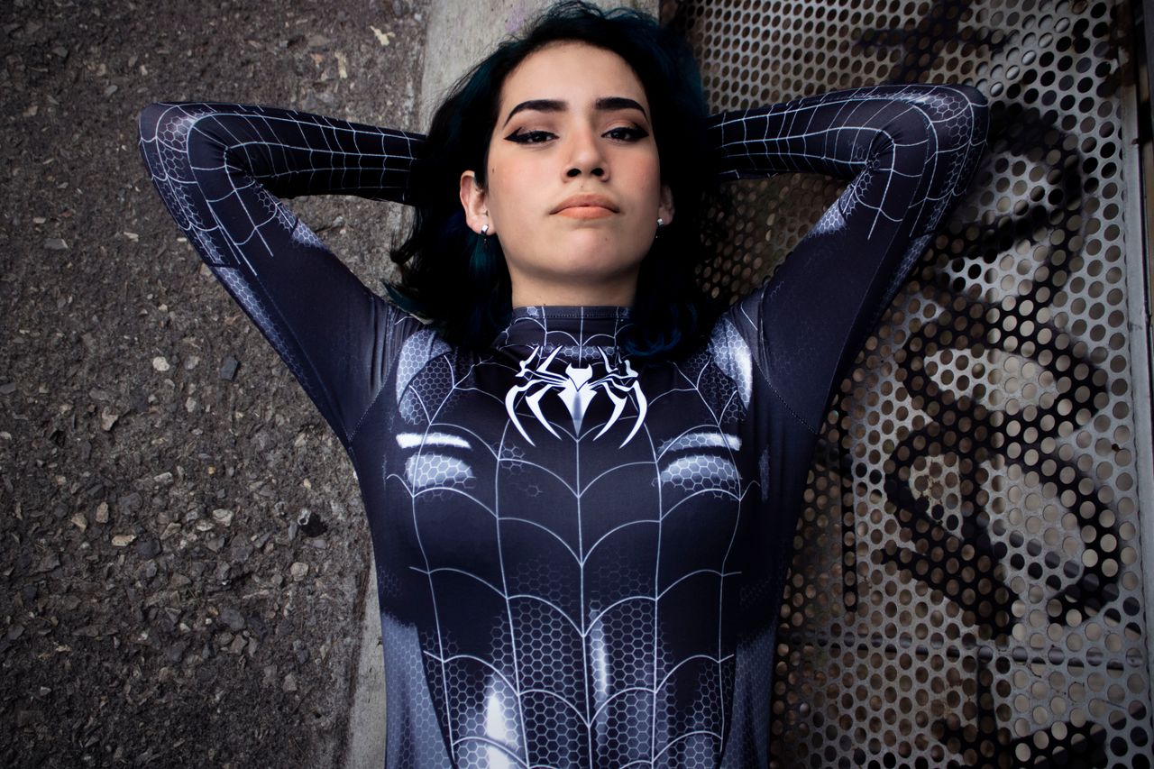 a woman in a spider man costume lying down outdoors embracing a superh