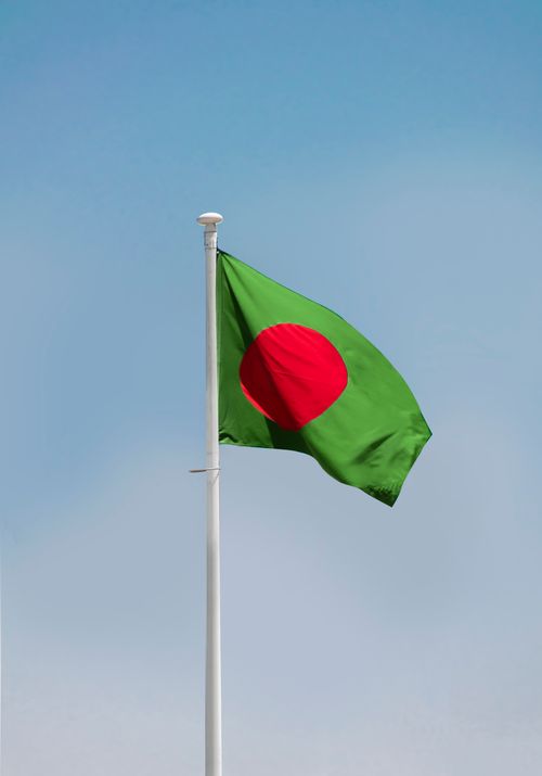 Free Bangladesh national flag waving on a flagpole against a clear blue sky in Dhaka. Stock Photo