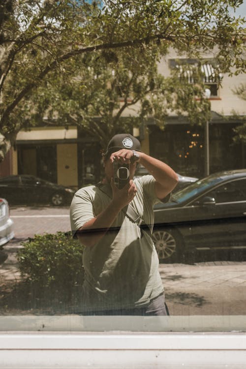 A Person in Gray T-shirt Outside Window Holding a Camera