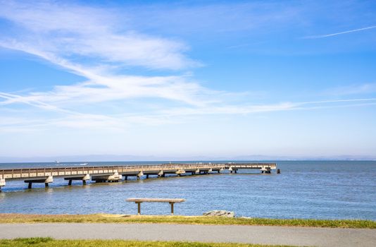 Tranquil view of a wooden pier reaching into the serene ocean under a clear blue sky.