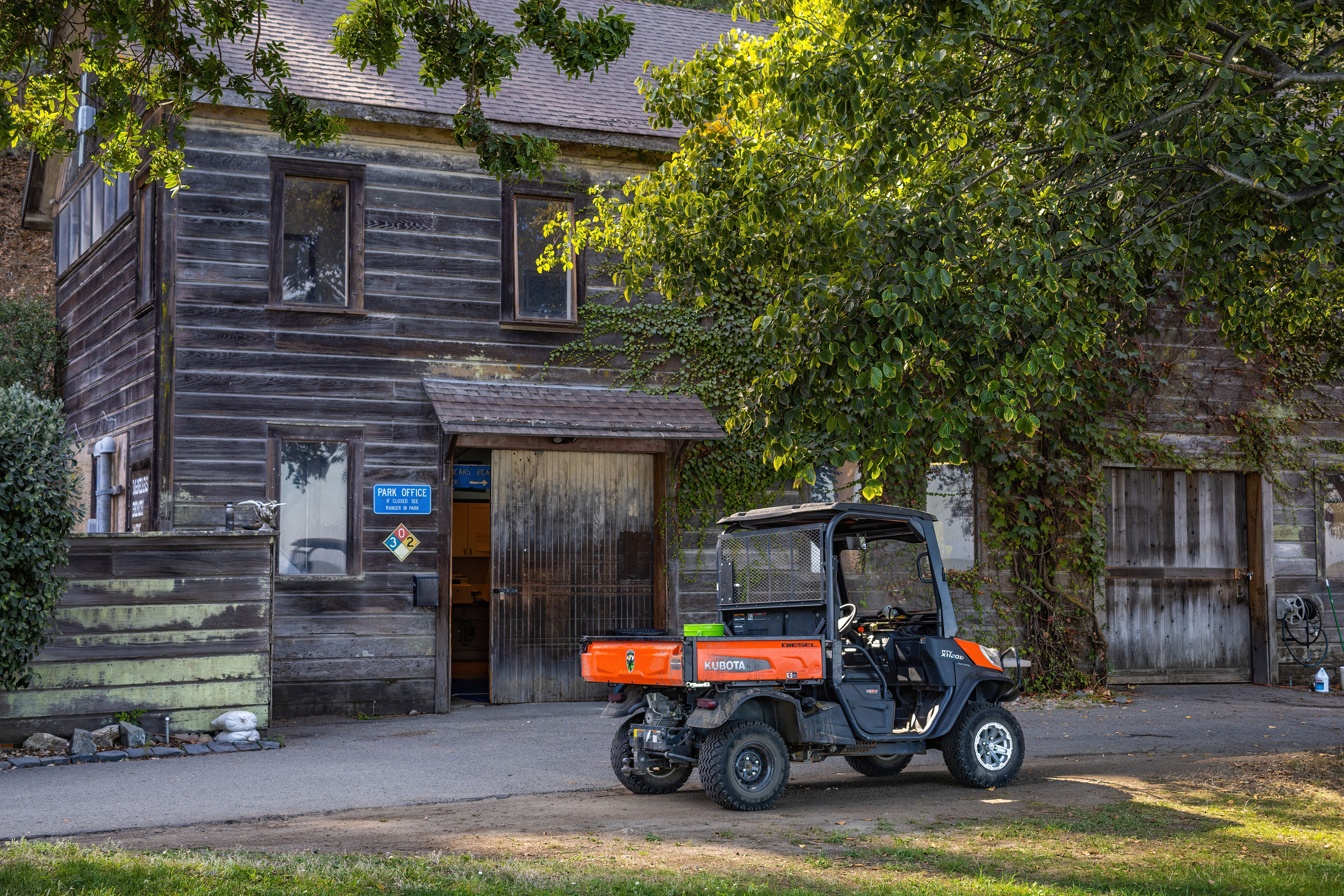 A rustic wooden park office with an orange utility vehicle parked outside amidst lush greenery.