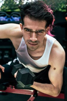 A determined man in a white tank top lifts a dumbbell, showcasing strength and fitness.