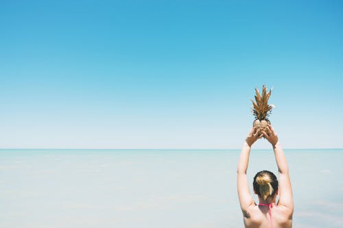 Woman Holding Pineapple Fruit Standing Near Body of Water