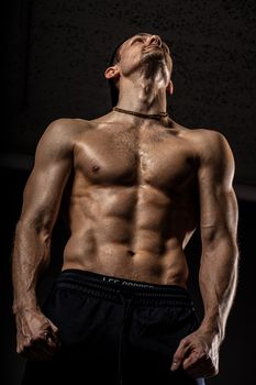 A shirtless muscular man poses confidently, looking upwards, showcasing fitness and strength.