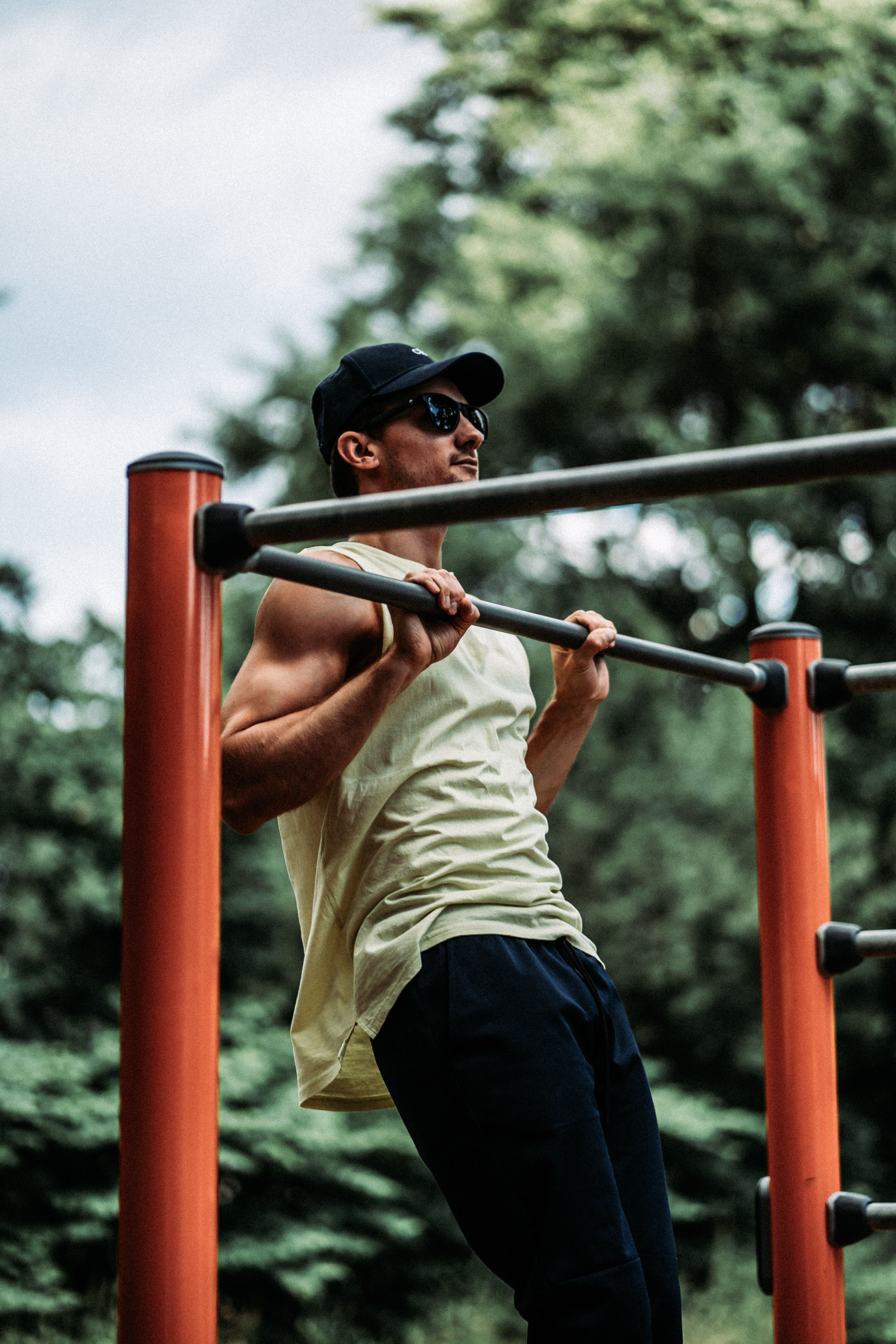 Man in white tank top exercising outdoors on metal bars.