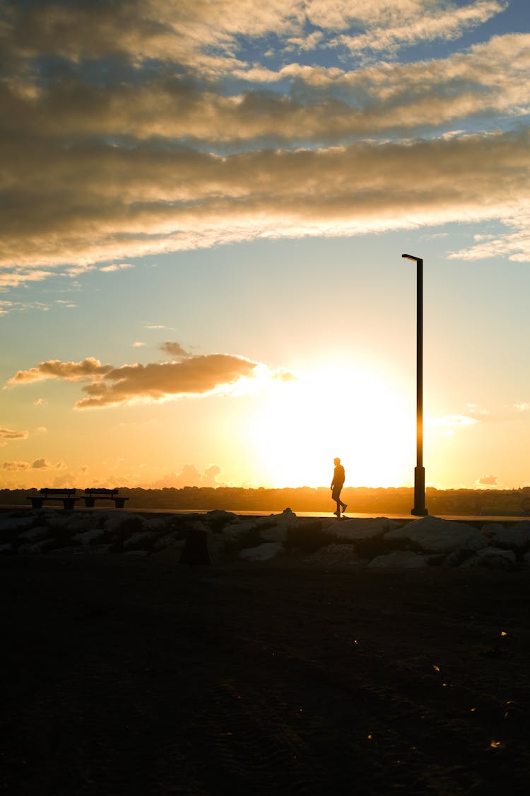 Silhouette Of A Person Walking Near A Lamppost During Golden Hour