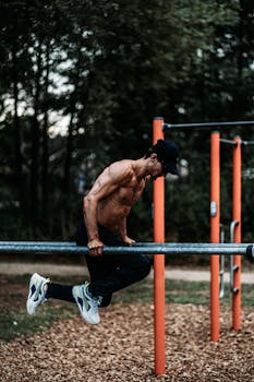 Shirtless man exercising on parallel bars in a park, showcasing muscular physique and fitness focus.