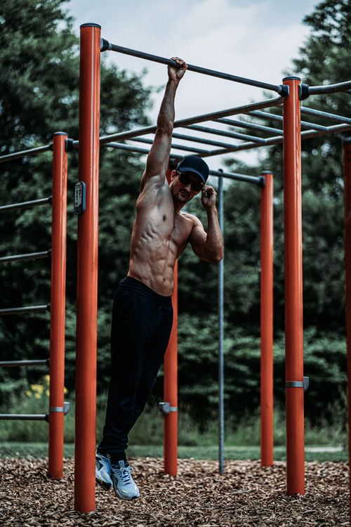 Free Muscular man hangs from monkey bars, showcasing strength and fitness outdoors. Stock Photo