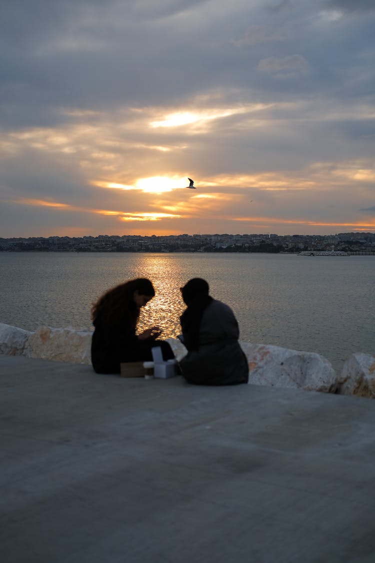 People Sitting On The Bay Near Big Rocks