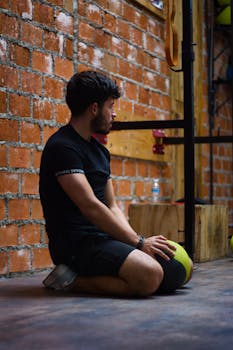 Adult man in athletic wear resting on gym floor with medicine ball.