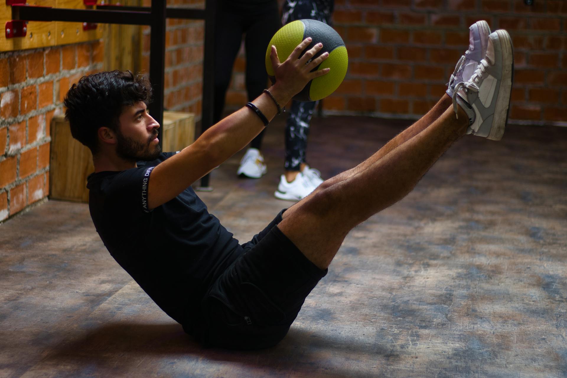 Focused man performing core exercises with a medicine ball in an indoor gym highlighting fitness and strength.