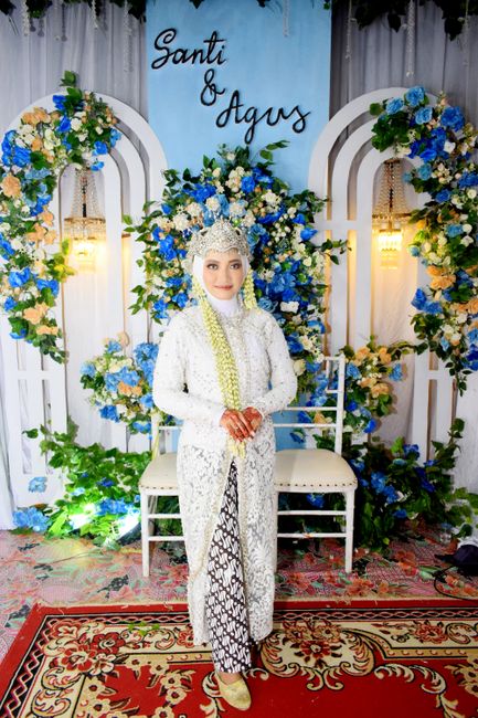 Bride in traditional attire with floral backdrop at a wedding.