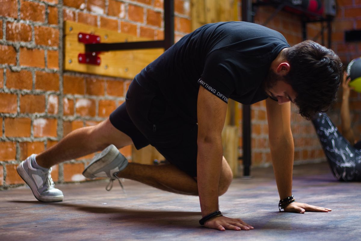 A man in a low crawling position on his hands and feet on a gym floor, one knee driven forward.