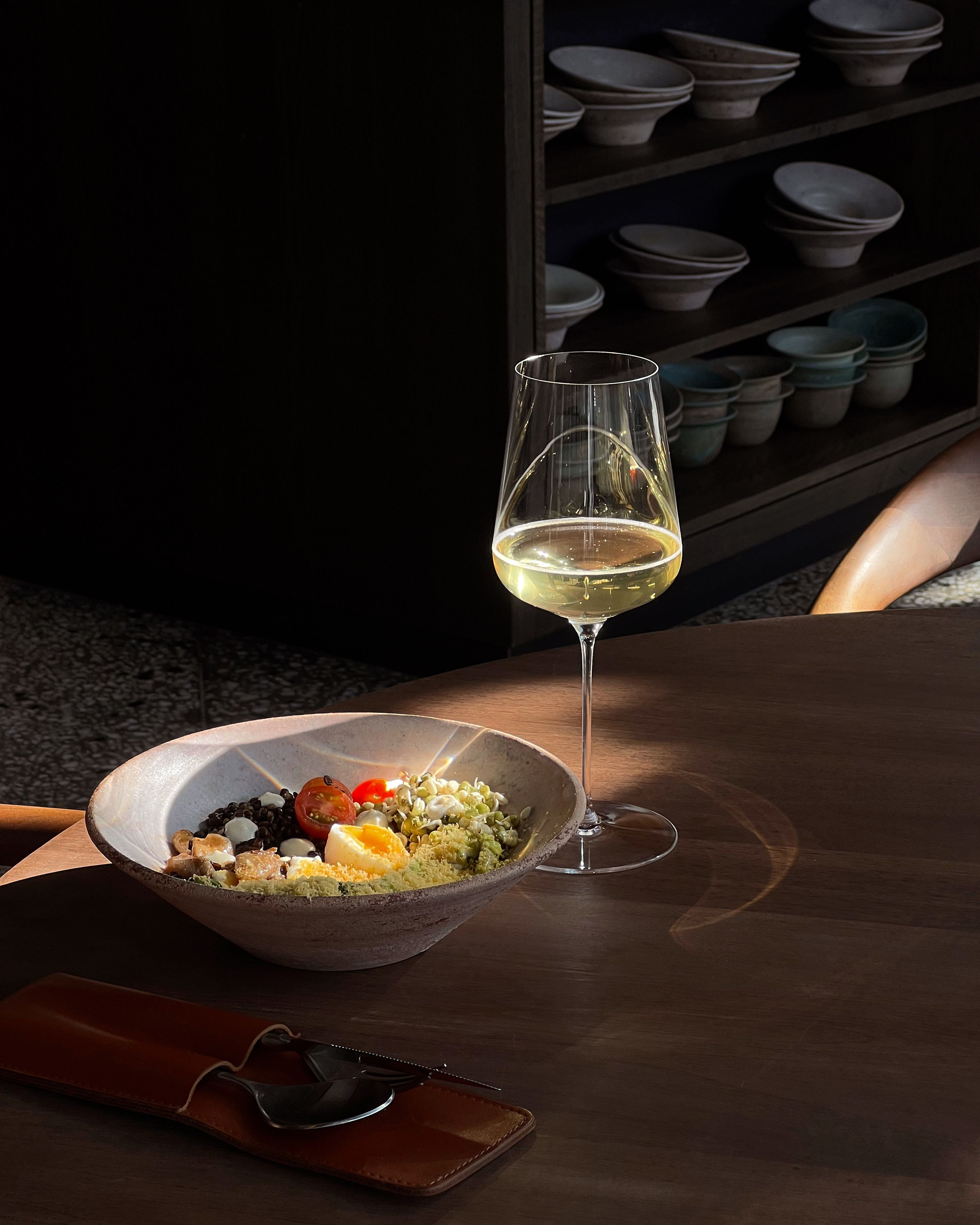 A fresh salad and glass of white wine on a wooden table, set for elegant indoor dining.