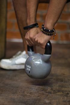 A person lifting a gray 25LB kettlebell in a gym setting, focusing on hands and equipment.