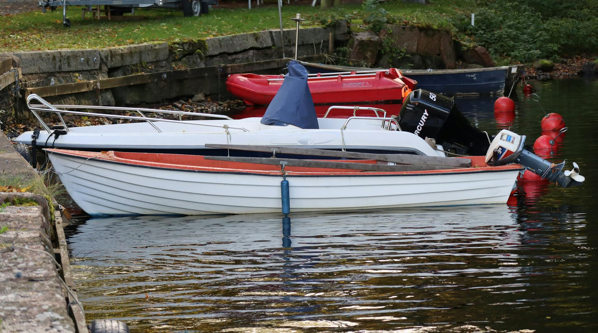 A docked motorboat featuring a Mercury engine near the riverside, surrounded by red buoy markers.