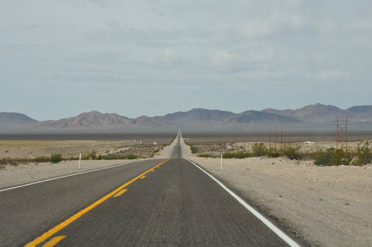 Landscape Of An Asphalt Road Through Empty Desert Towards Mountains 