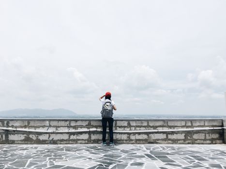 A person with a backpack and red hat enjoys a scenic view from a stone platform.