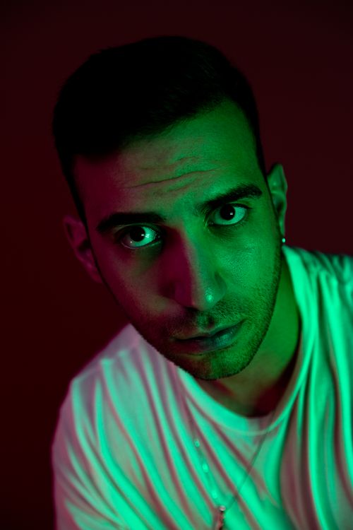Free Striking portrait of a young man with intense gaze, highlighted by green and red lighting effects. Stock Photo
