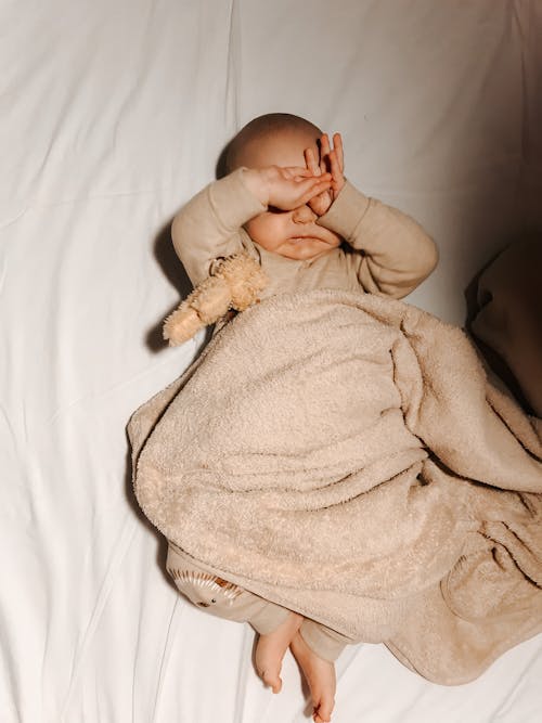 Free A Baby Sleeping on the Bed with Brown Blanket Covering Her Body Stock Photo