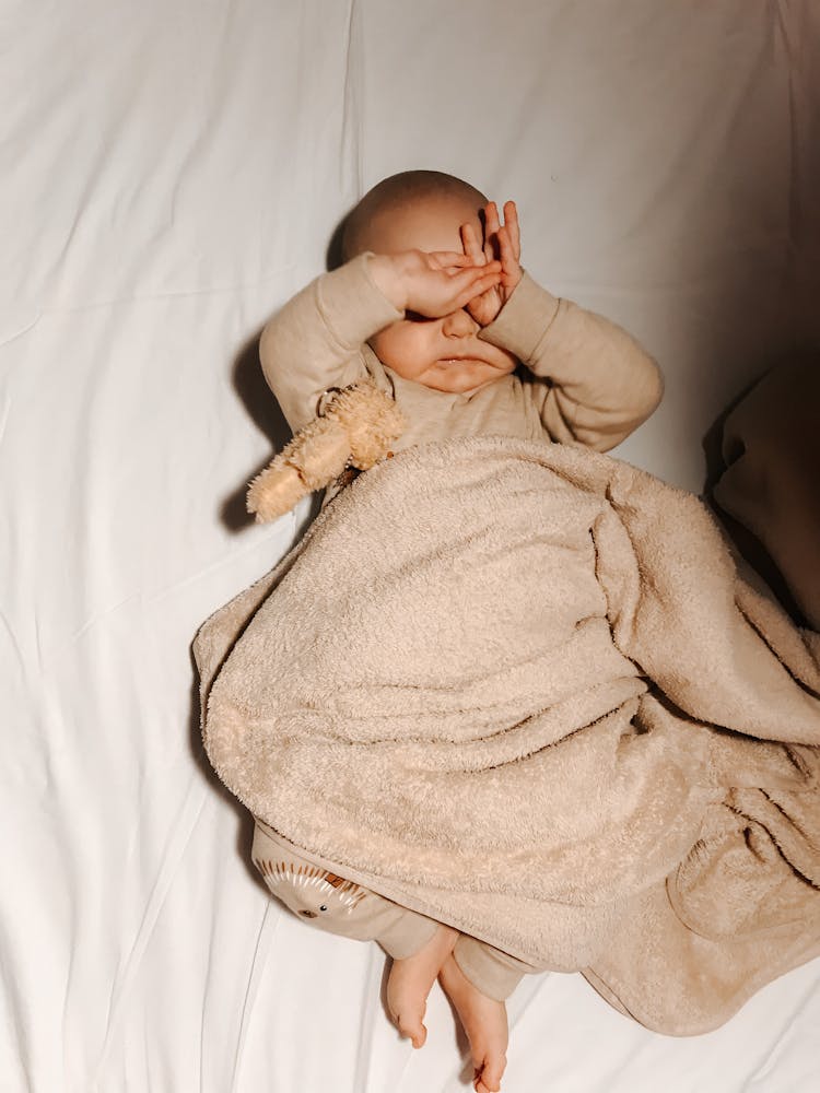 A Baby Sleeping On The Bed With Brown Blanket Covering Her Body