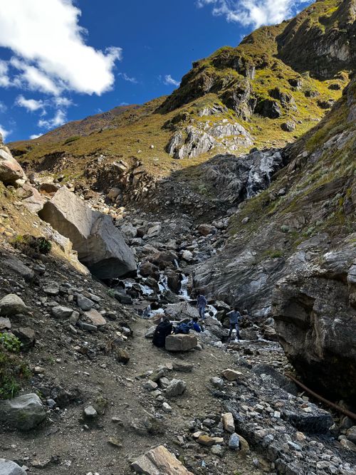 Free Hikers exploring a rocky mountain landscape with a stream, under a bright sky. Stock Photo