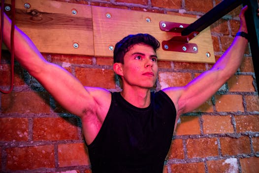 Focused young man exercising with gym equipment against a brick wall indoors.