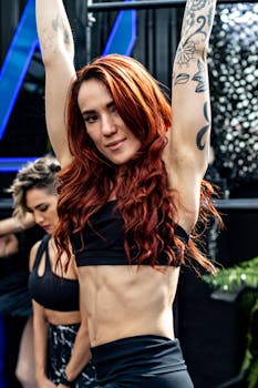 Fit woman with tattoos working out at a gym, showcasing muscular arms and red hair.