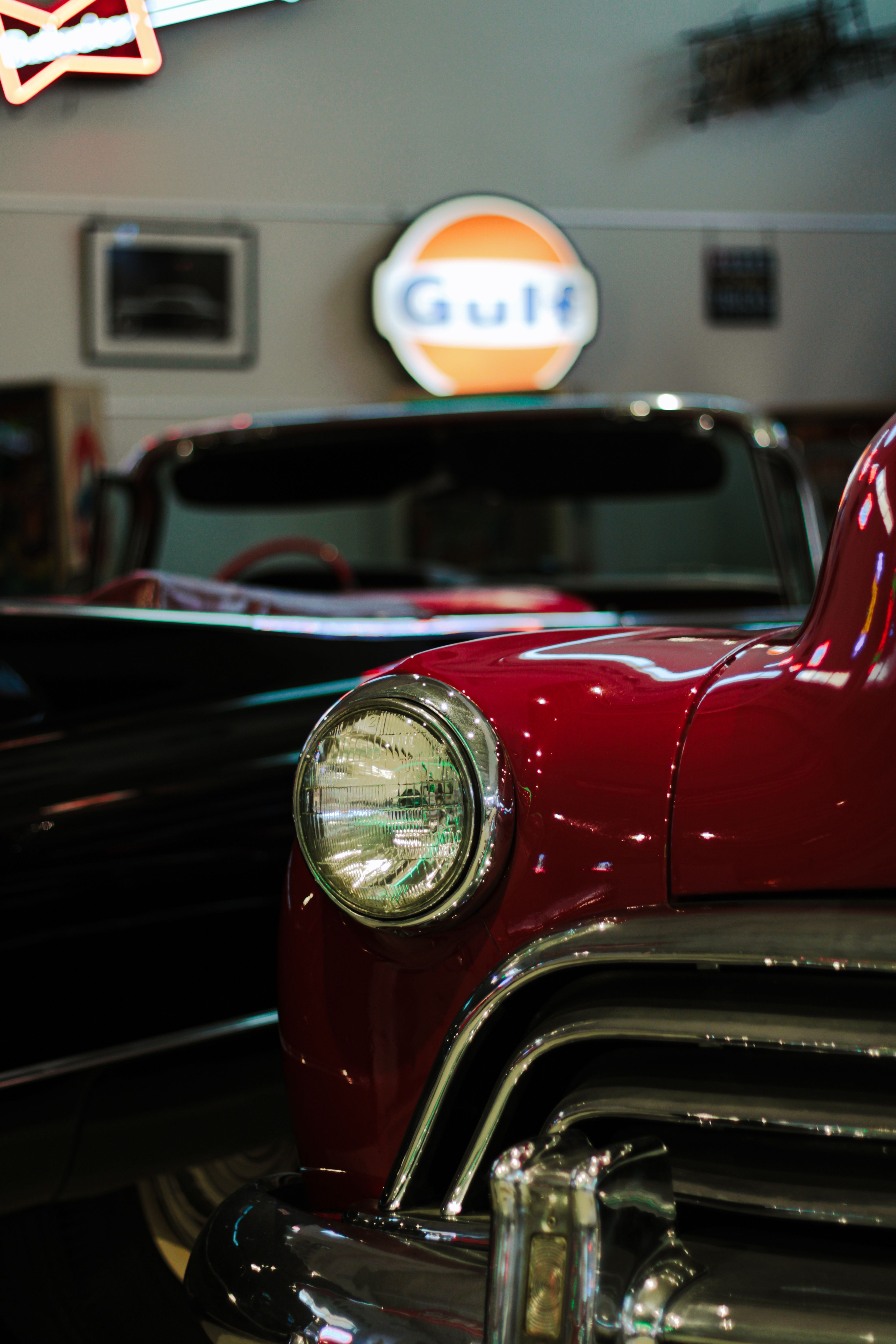 Close-up of a classic red vintage car's headlight indoors with retro Gulf sign.