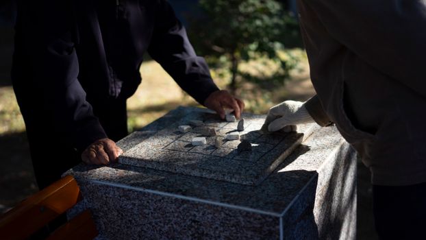 Two people play an outdoor strategy game using stones on a marble table.