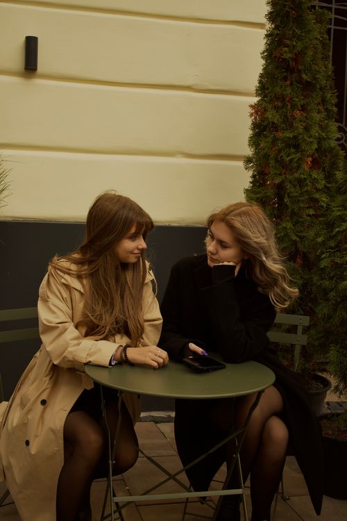 Free Two women sit outside a café, engaged in conversation at a small table. Stock Photo