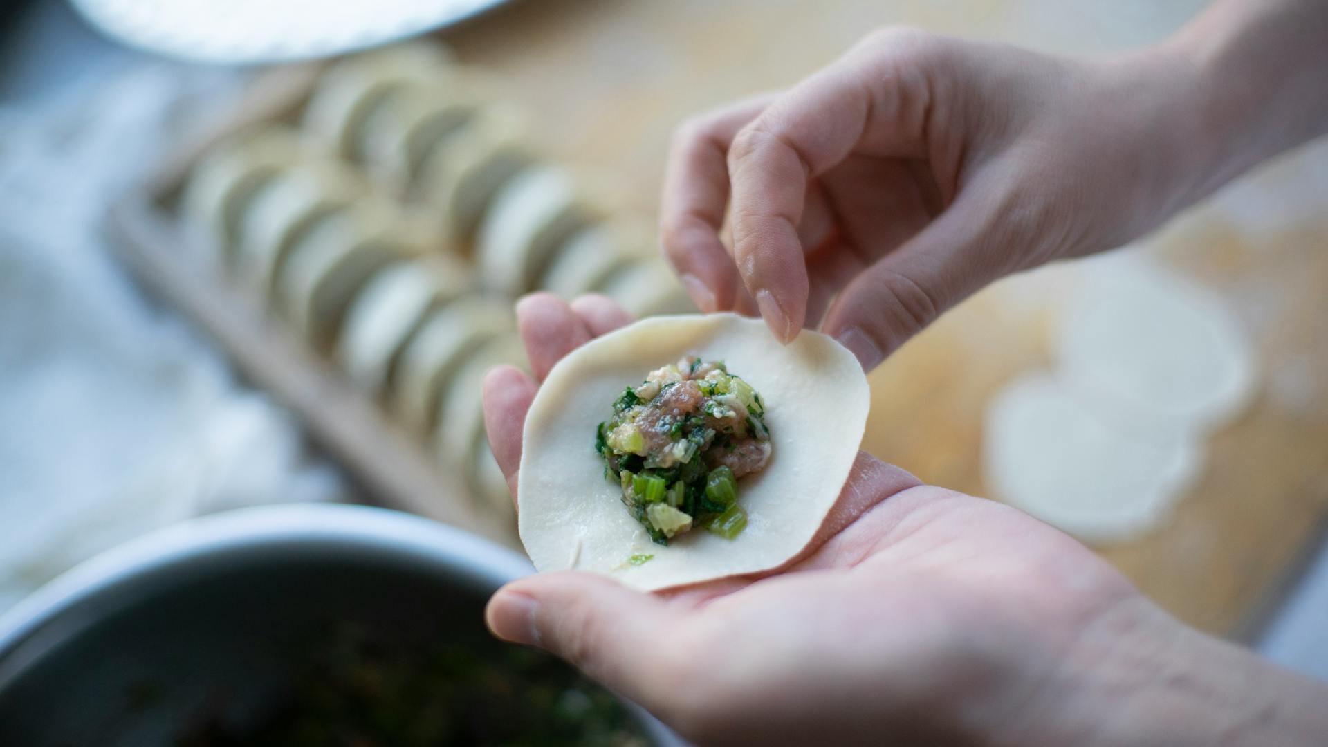 Hands carefully wrapping dumpling with savory filling, showcasing detailed food preparation.
