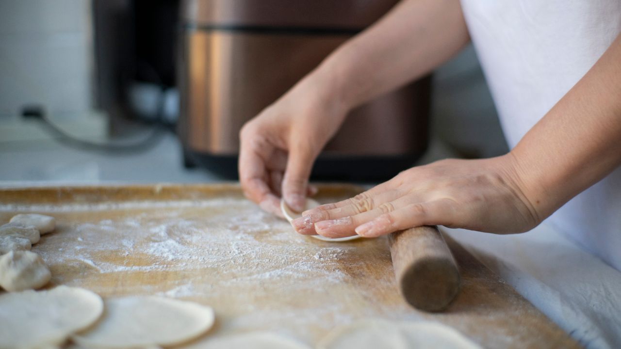 Hands rolling small dough discs with a short rolling pin on a floured board
