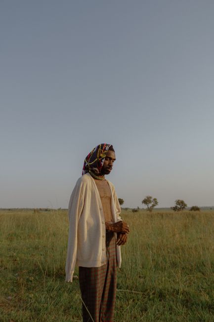 Fashionable man wearing a colorful headscarf standing in a serene field at dusk.