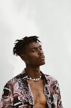 Portrait of a young man with dreadlocks wearing a trendy floral shirt against a white background.