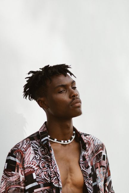 Portrait of a young man with dreadlocks wearing a trendy floral shirt against a white background.