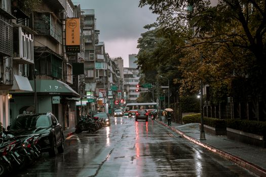 A rainy day on a bustling urban street with cars, pedestrians, and wet pavement.