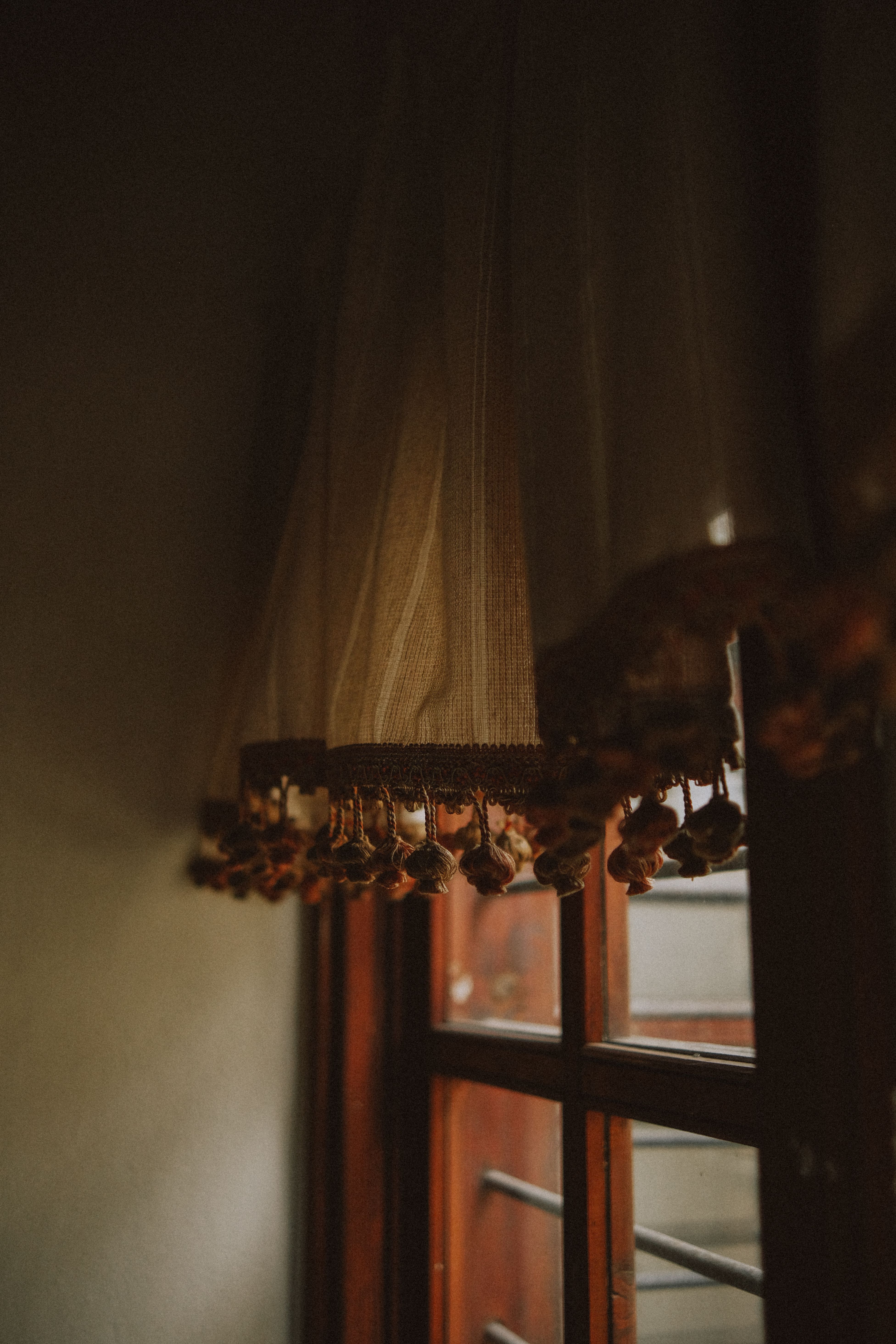 Softly lit vintage curtain with tassels hanging by a wooden window indoors.