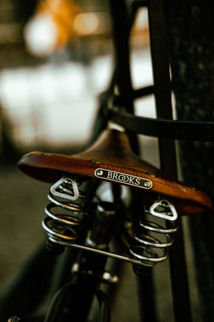 Detailed view of a classic Brooks leather bicycle seat with springs, photographed outdoors.