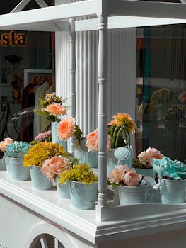 A beautiful display of assorted flowers in pastel pails on a classic white stand indoors.