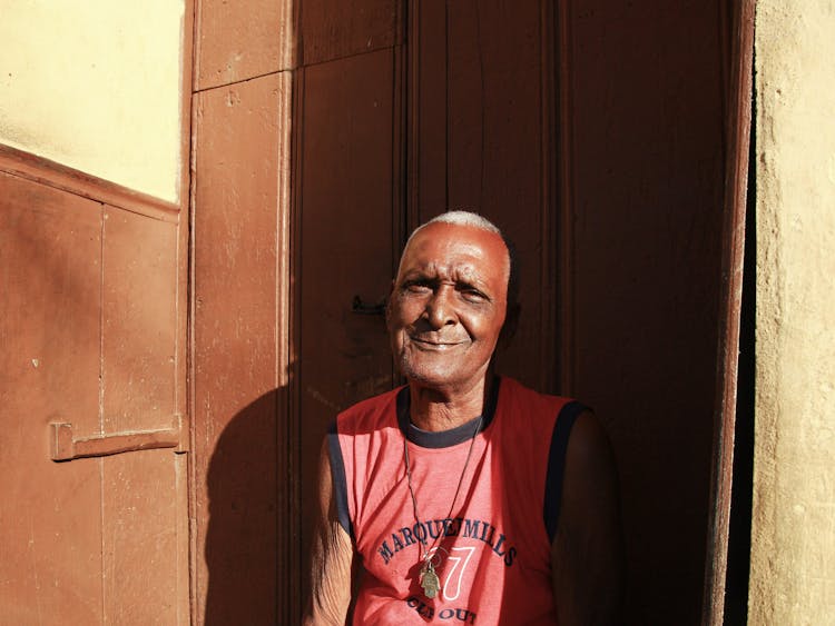 Man In Red Tank Top Sitting In Front Of The Doorway