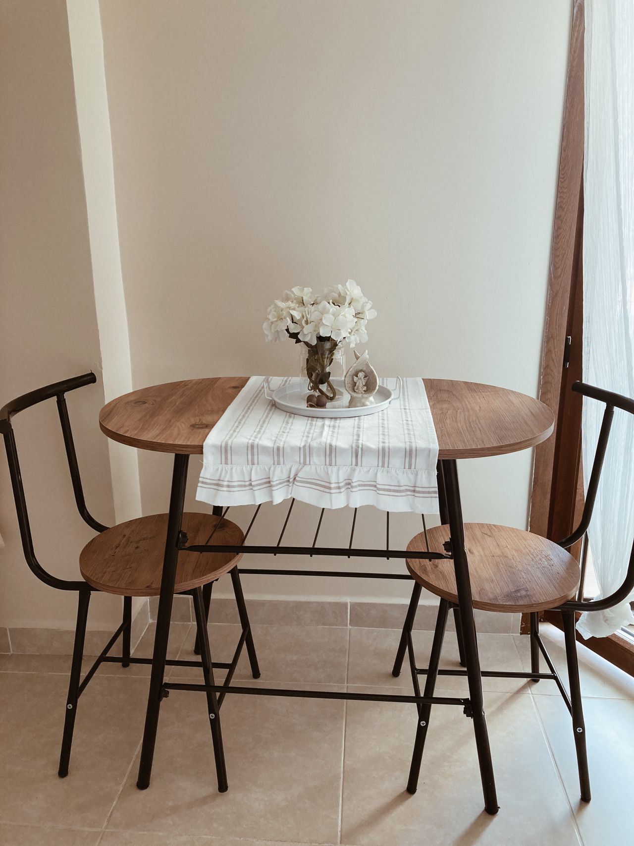 Small oval wooden table for two with black metal chairs and a table runner